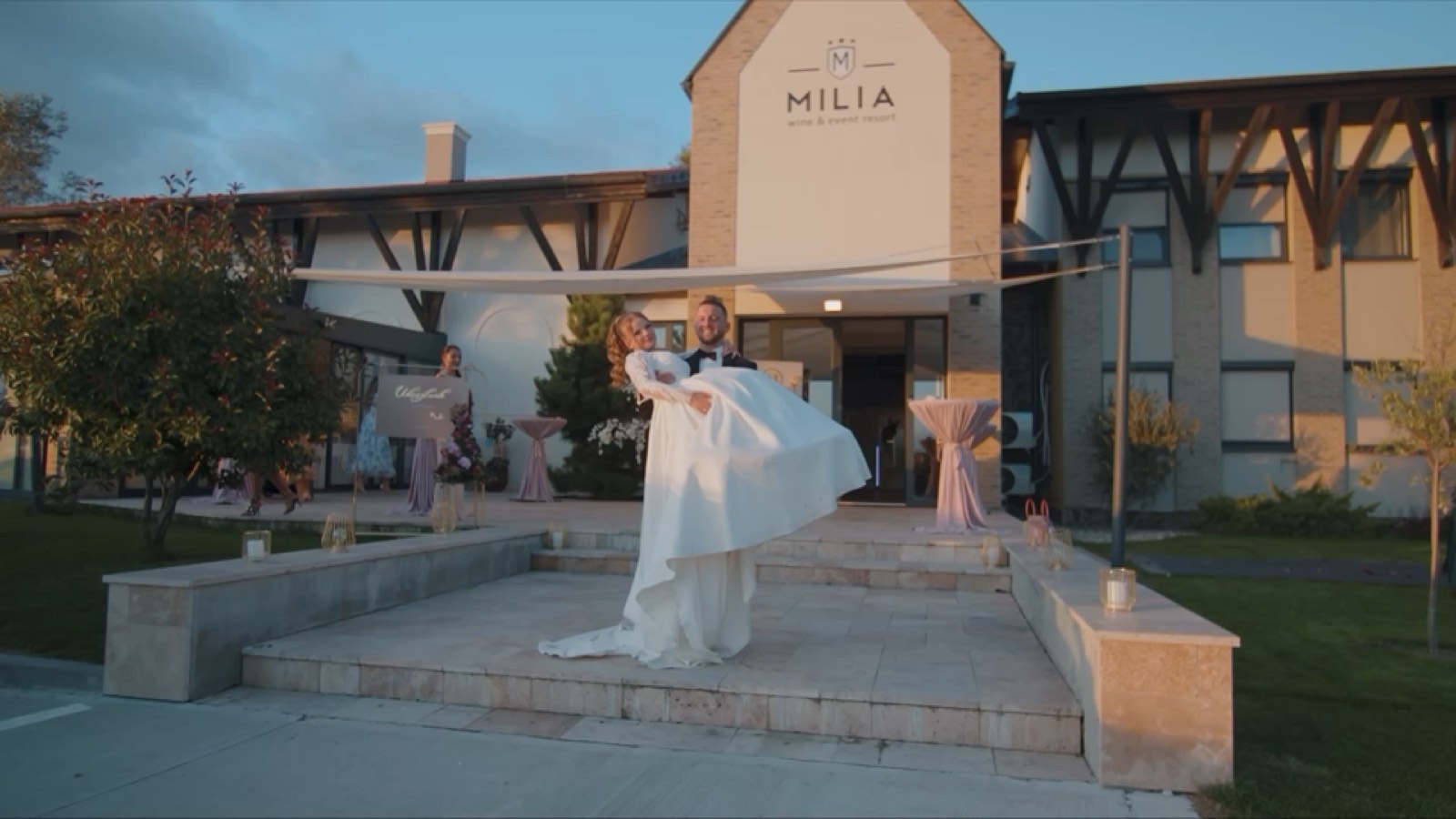 A groom carries his bride in front of the Mília resort during golden hour